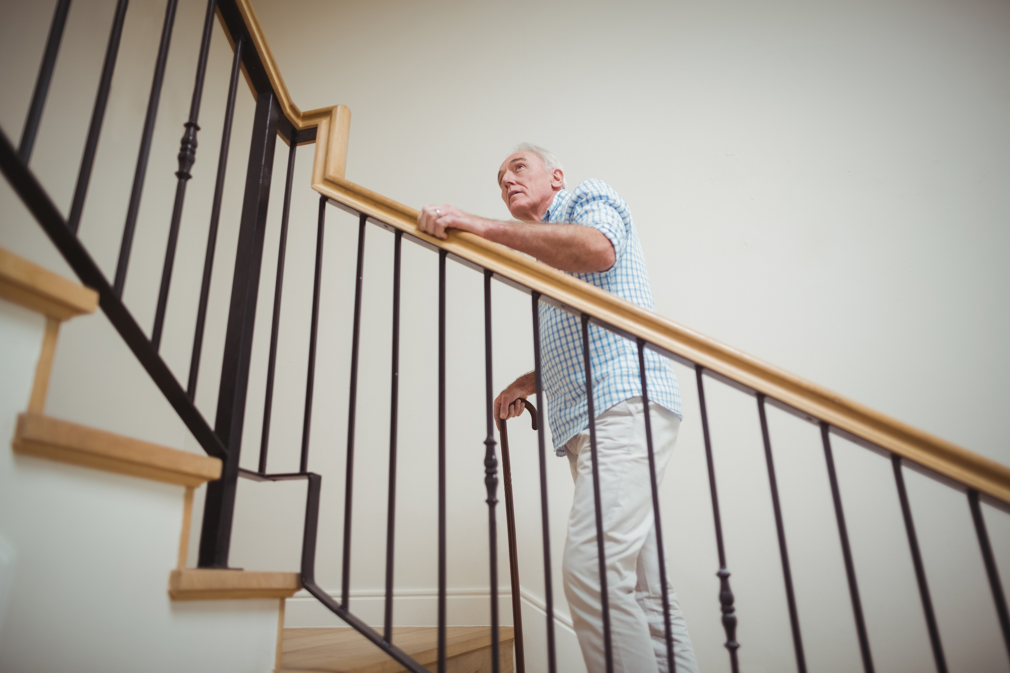 An older man climbing a staircase at home with a handrail and cane