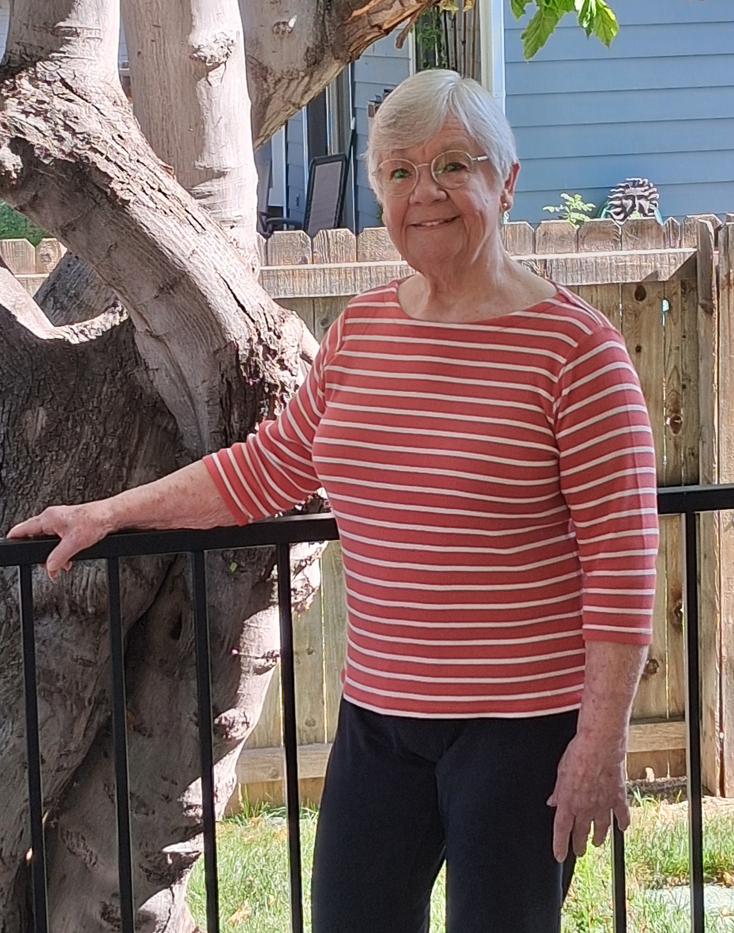 Steffani M., a movement coaching client, standing by a tree in her garden