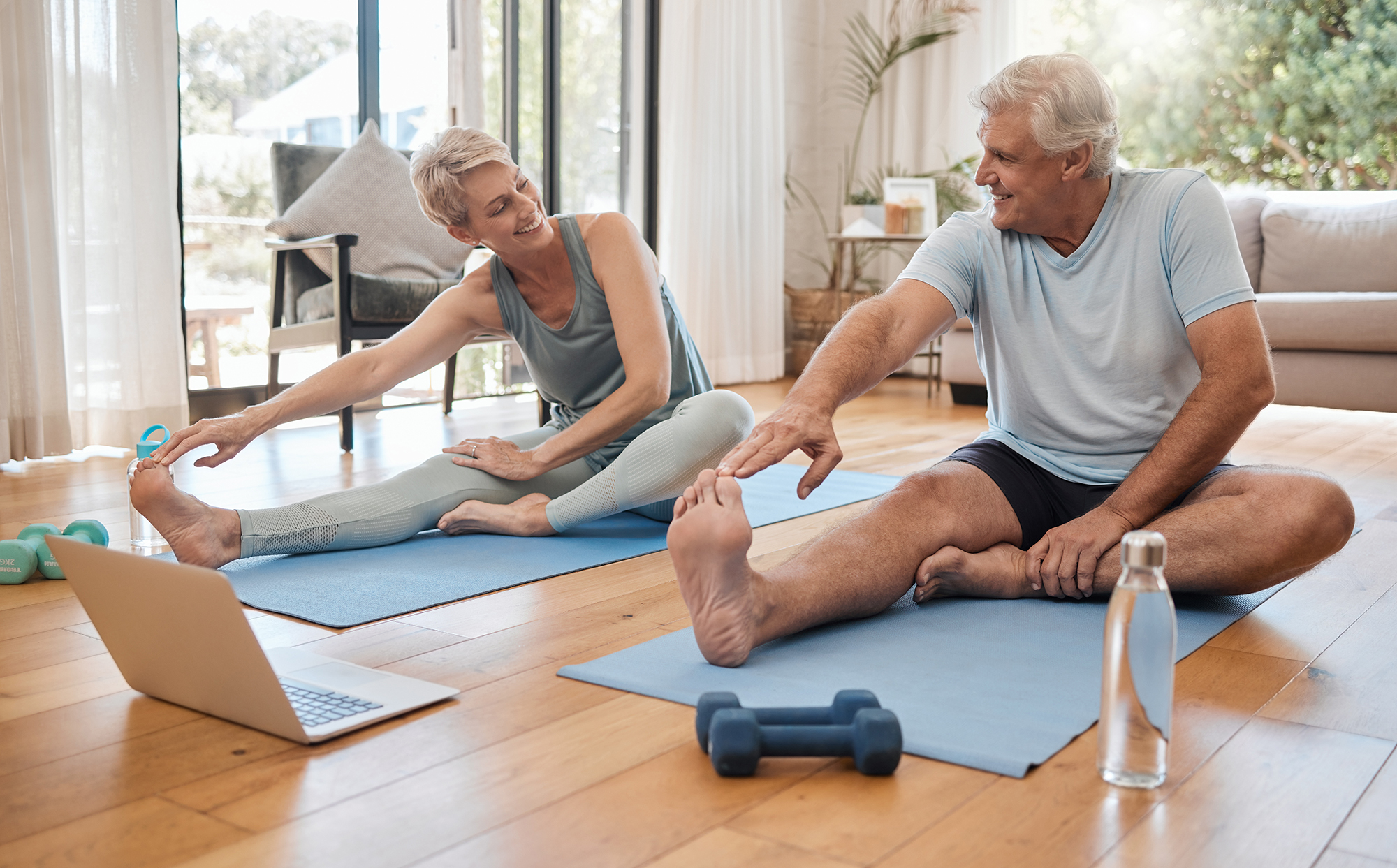 An older couple stretching together on mats in their living room