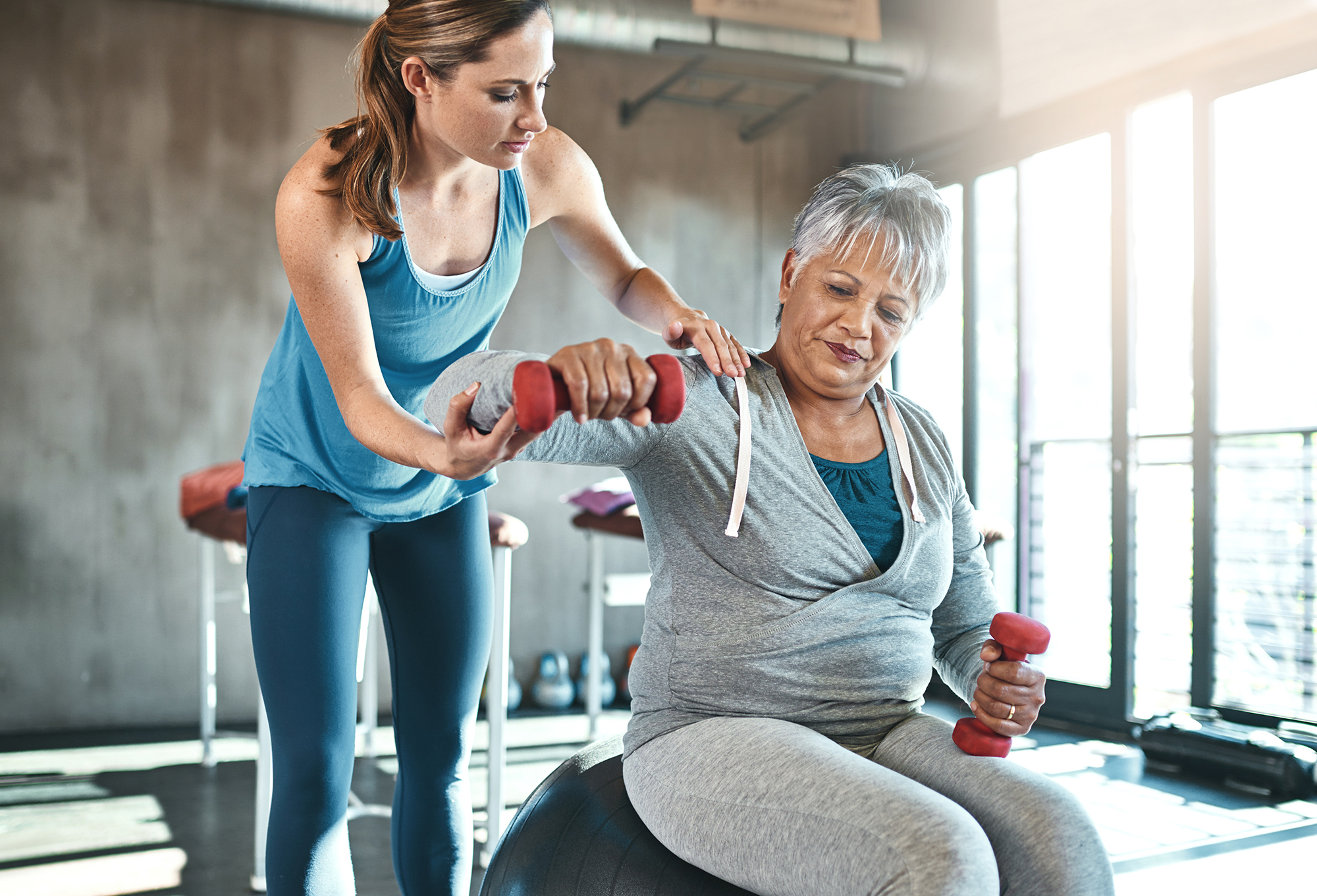 A coach guiding an older woman through a light dumbbell exercise